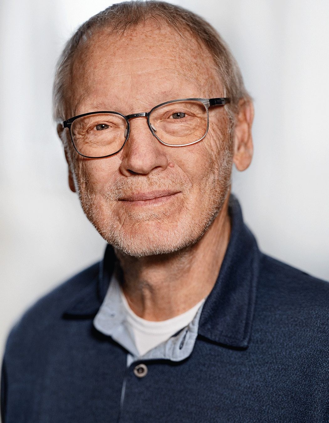 Photo of Breakthrough Prize laureate, physician Jens Juul Holst against a white background. He wears a blue shirt and smiles.