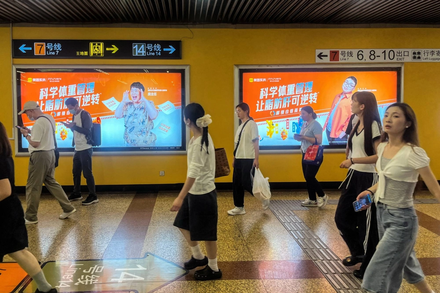 People walk past billboards from Innovent Biologics and Meituan displayed on a wall in a metro station in Shanghai on July 6.