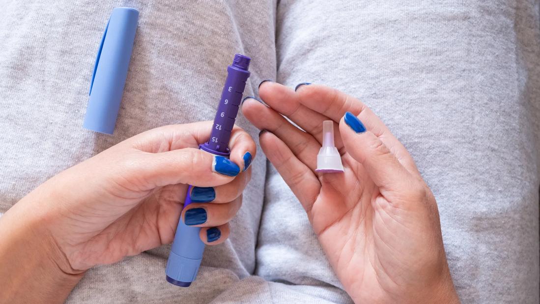 Person holding medication injector in lap with their hands